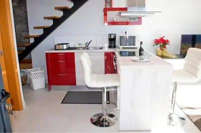 a kitchen with white counter chairs and red cabinets at Crystal House in Calheta