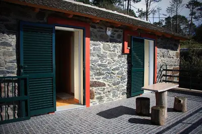 a stone house with green doors and a wooden bench at Raposeira Chloe T2 in Fajã da Ovelha