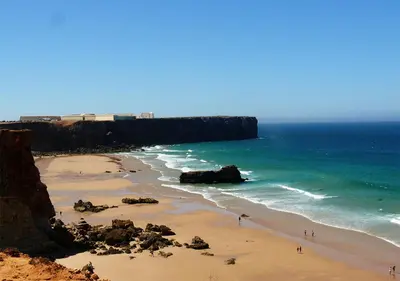 a beach with people walking on the sand and the ocean at Parque de Campismo Orbitur Sagres in Sagres