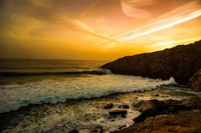 a sunset over the ocean with a rocky beach at Hostel on the Hill in Raposeira