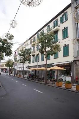 an empty street with a building with tables and umbrellas at The Marketplace by Storytellers in Funchal
