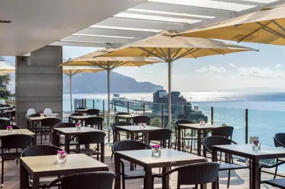 a restaurant with tables and chairs and a view of the ocean at Pestana Madeira Beach Club in Funchal
