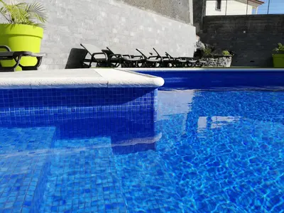 a blue swimming pool with chairs and a table at Imaculado Village in Funchal