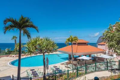 a resort pool with palm trees and the ocean at Pestana Royal All Inclusive Ocean & Spa Resort in Funchal