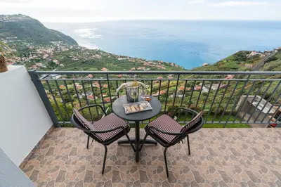 a table and chairs on a balcony with a view of the ocean at Casa da Tenda in Arco da Calheta