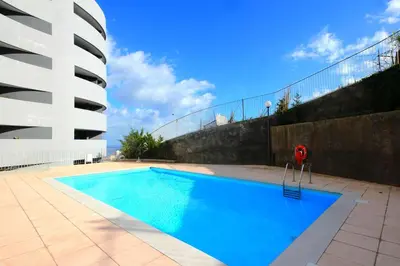 a swimming pool with a red chair next to a building at Virtudes Ocean view with pool by Holiday Rental Madeira in Funchal