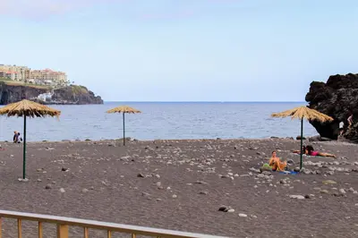 a beach with umbrellas and people laying on the sand at Vista Formosa Funchal in Funchal