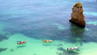 three boats in the water near a rock formation at Bel appartement au bord de la mer de Porto de Mos in Lagos