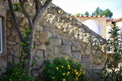 a stone wall with a tree and yellow flowers at Casinhas da Figueira in Budens
