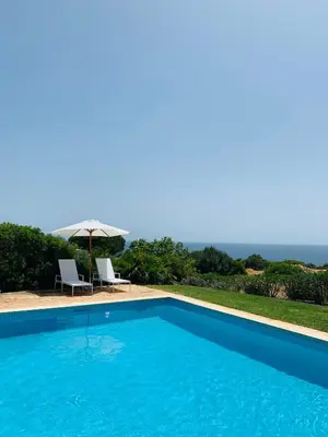 a swimming pool with two chairs and an umbrella at Dona Maria 66 in Luz