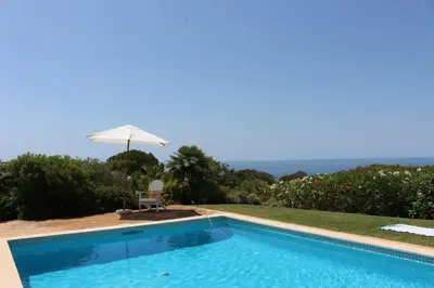 a swimming pool with an umbrella and a chair at Dona Maria 66 in Luz