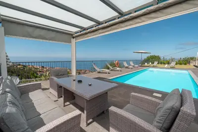 a patio with a table and chairs and a swimming pool at Villa Panoramica II in Arco da Calheta