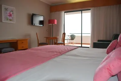 a bedroom with a bed with pink sheets and a television at Hotel Jardim Atlantico in Calheta