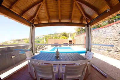 a patio with a table and chairs and a swimming pool at Casa da Rainha Bungallow in Estreito da Calheta