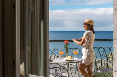 a woman standing on a balcony with a table with wine glasses at Enotel Sunset Bay in Ponta do Sol