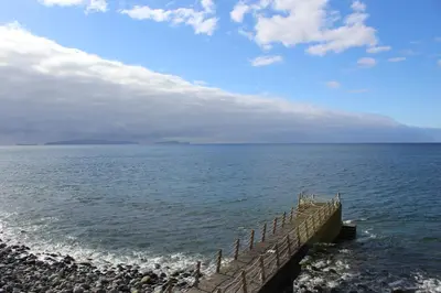 a wooden pier in the ocean with a cloudy sky at Refugio Madeira in Caniço
