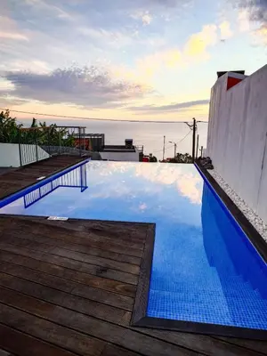 a large swimming pool with a wooden deck and the ocean at Casa das Andorinhas in Estreito da Calheta