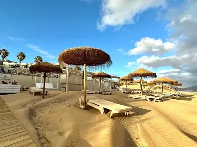 a beach with tables and straw umbrellas on the sand at Paradise Beach in Porto Santo