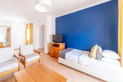 a bedroom with a blue wall and a bed and a chair at Oasis Beach Apartments in Luz