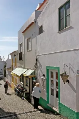 a woman walking past a building on a street at Apartamentos Os Descobrimentos in Burgau