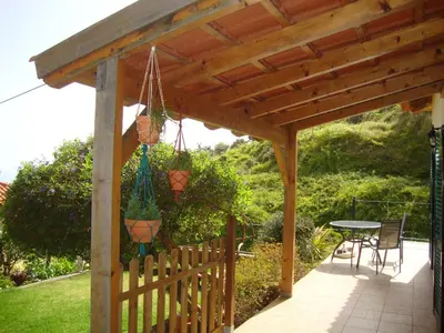 a wooden pergola with a table and chairs on a patio at Blooming Botanic Houses in Estreito da Calheta