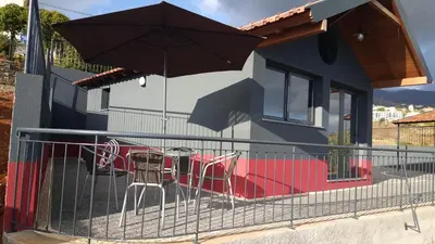 a table and chairs in front of a house with an umbrella at Adega do Avô 2 Madeira in Estreito da Calheta