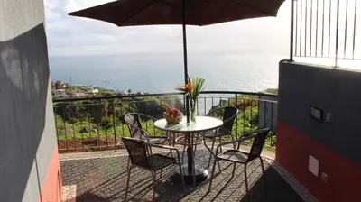 a table and chairs on a balcony with an umbrella at Adega do Avô 2 Madeira in Estreito da Calheta