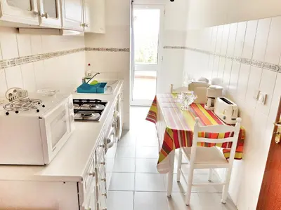 a kitchen with white appliances and a table and chairs at Falesia Apartment - Reis Magos Beach in Caniço
