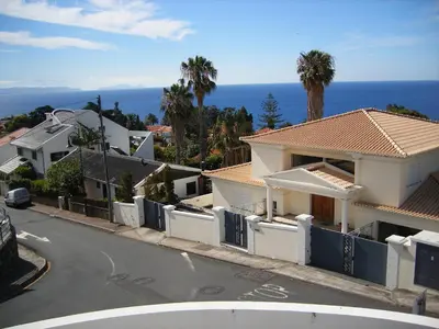 a white house with a fence and palm trees at Vila Faia in Caniço