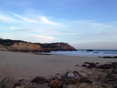a beach with rocks on the sand and the ocean at Trivial Pisão - Casa de Férias, para a sua Família in Raposeira