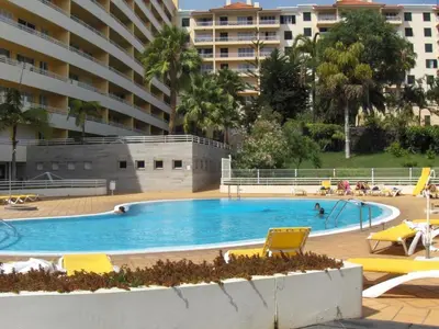 a swimming pool with yellow chairs and a large building at Enzo Apartament in Funchal