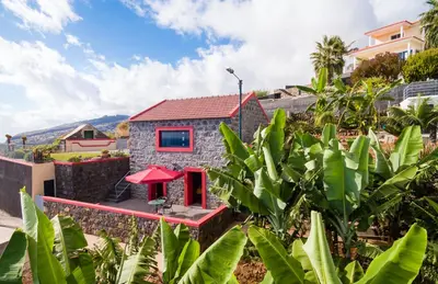 a tiny house with a red door in a garden at Endless Blue House in Arco da Calheta