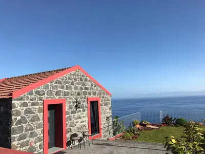 a small stone house with red windows and the ocean at Endless Blue House in Arco da Calheta