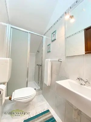 a white bathroom with a toilet and a sink at Gardens Guest House in São Vicente
