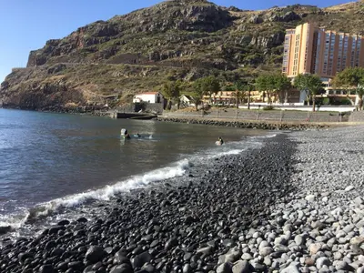 a rocky beach with people swimming in the water at Estacada Apartment in Machico