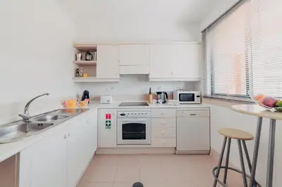 a white kitchen with white appliances and a table at Funchal Lounge Apartment by Amazing Madeira in Funchal