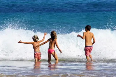 three children are playing in the water at the beach at Porto Santo - Pedras Pretas Beach House in Porto Santo