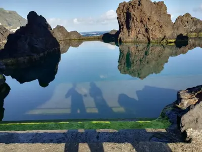 a reflection of a man and his shadow in the water at Casa da Grota in Porto Moniz