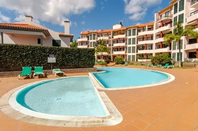 a swimming pool with two chairs and a building at Varandas Funchal-Near center in Funchal