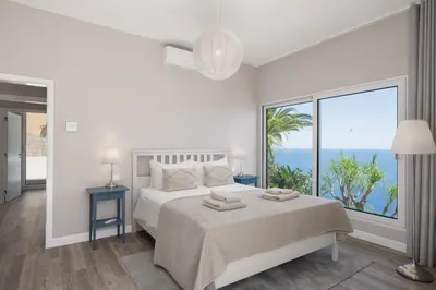 a white bedroom with a bed with a large window at OurMadeira - Villa Aquarela in Caniço