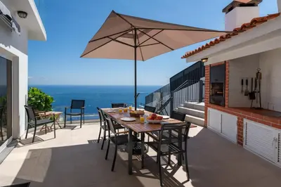 a table and chairs on a balcony with an umbrella at OurMadeira - Villa Aquarela in Caniço