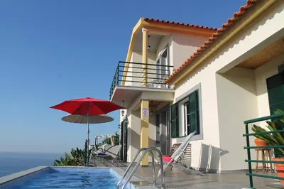 a house with a pool and a red umbrella at OurMadeira - Casa Jardim Mar in Ponta do Sol