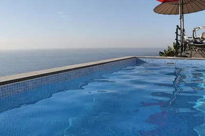 a swimming pool next to the ocean with an umbrella at OurMadeira - Casa Jardim Mar in Ponta do Sol