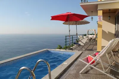 a swimming pool with chairs and a red umbrella at OurMadeira - Casa Jardim Mar in Ponta do Sol