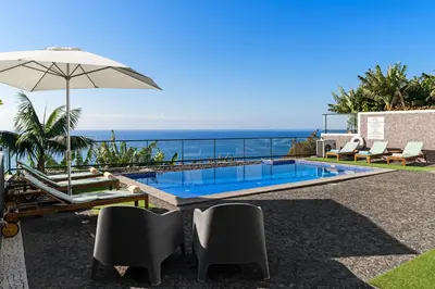 a swimming pool with chairs and an umbrella and the ocean at OurMadeira - Grayci's House in Arco da Calheta
