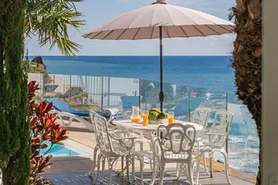 a table and chairs with an umbrella and the ocean at OurMadeira - Villa do Mar II in Arco da Calheta