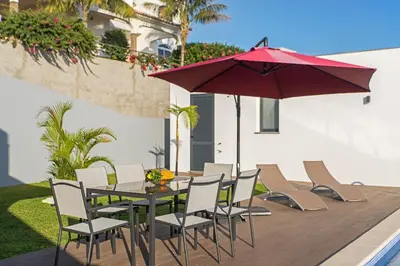a table and chairs with a red umbrella on a deck at Searenity Vacation Home I by An Island Apart in Arco da Calheta