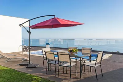 a table with chairs and a red umbrella next to a pool at Searenity Vacation Home I by An Island Apart in Arco da Calheta