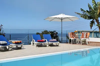a pool with chairs and a table and an umbrella at OurMadeira - Villa do Mar III in Arco da Calheta