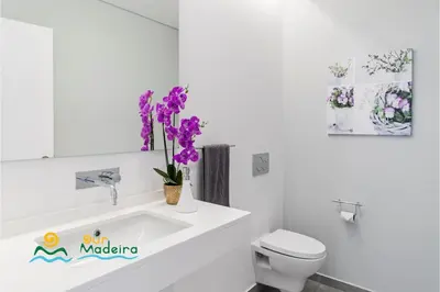 a bathroom with a sink and a toilet and purple flowers at OurMadeira - Calheta Heights in Calheta
